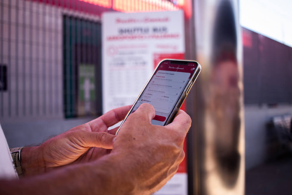 Mani che usano uno smartphone per prenotare un servizio navetta.